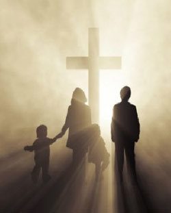 A family holding hands standing in front of a cross